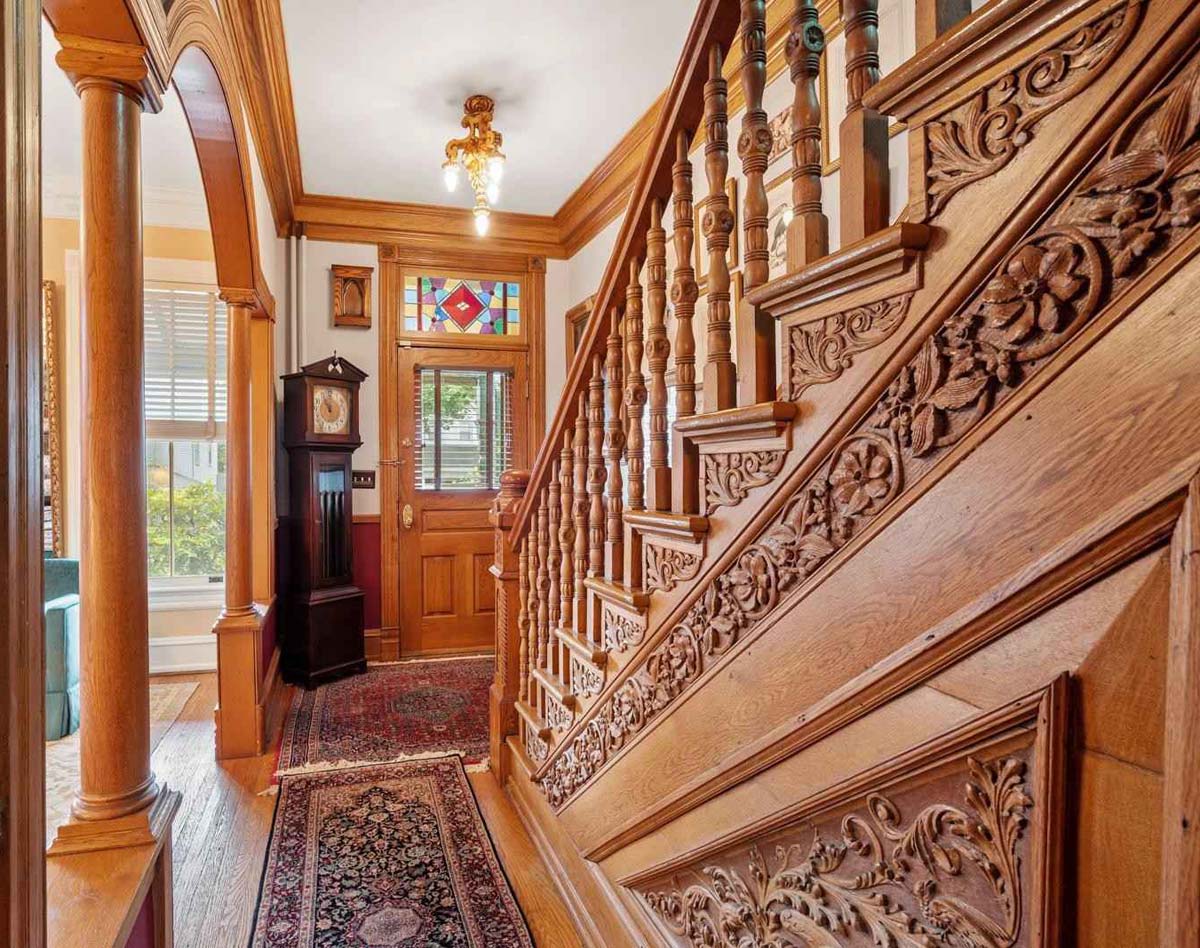 entry hall: front door with stained glass transom, ornately carved staricase, wooden arch into parlor