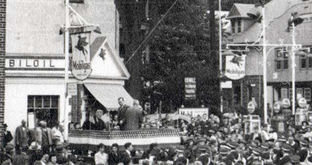 Mobil gas station surrounded by a crowd, speaker platform in front