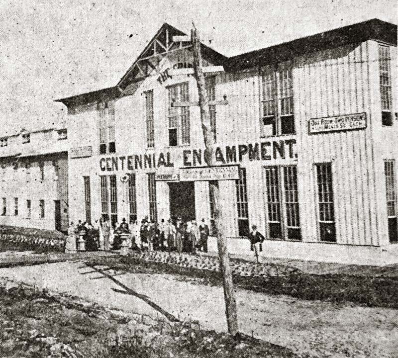 A group of about 20 dressed in waistcoats, tophats and bustles stands before the entrance of the encampment hotel