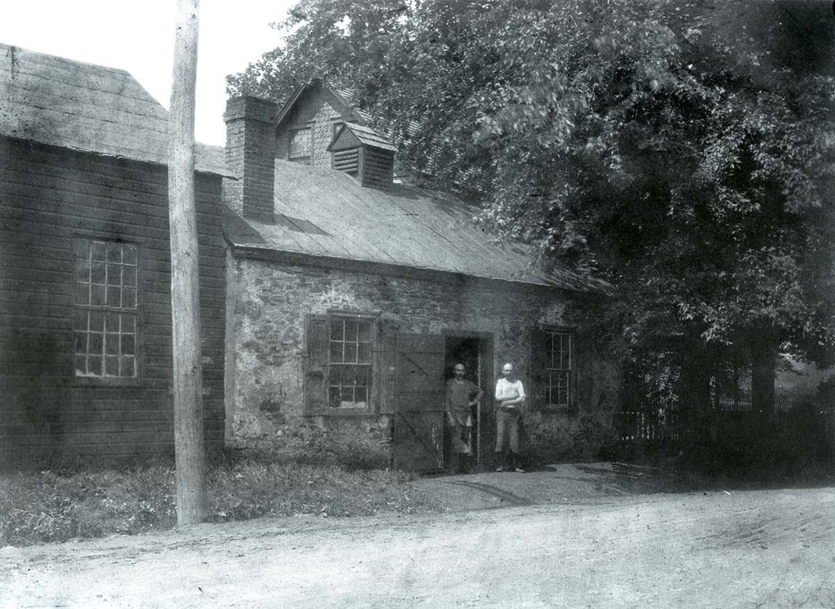 Two men stand in the doorway of the stone blacksmith shop