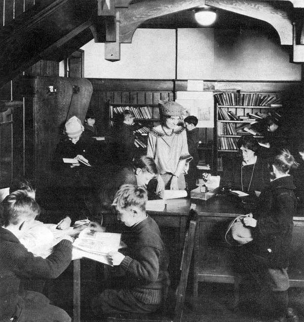 2 women at desk surrounded by children reading