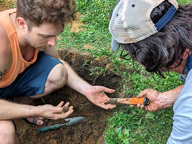 man on right waves a handheld metal detector over an object held by man on left
