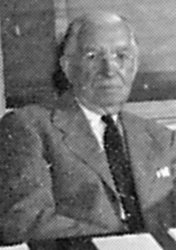 white-haired man seated in suit with glasses