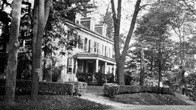 large federal-style house behind a hedge