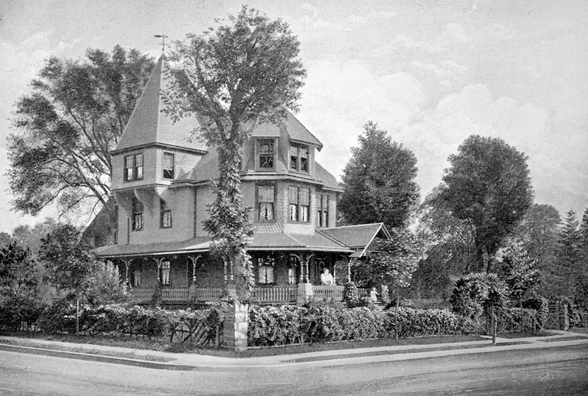 A lithograph of a three-story house with a square turret and wraparound porch, surrounded by a fence covered with plantings. A woman looks out from the porch, and a small child gestures from the front steps.